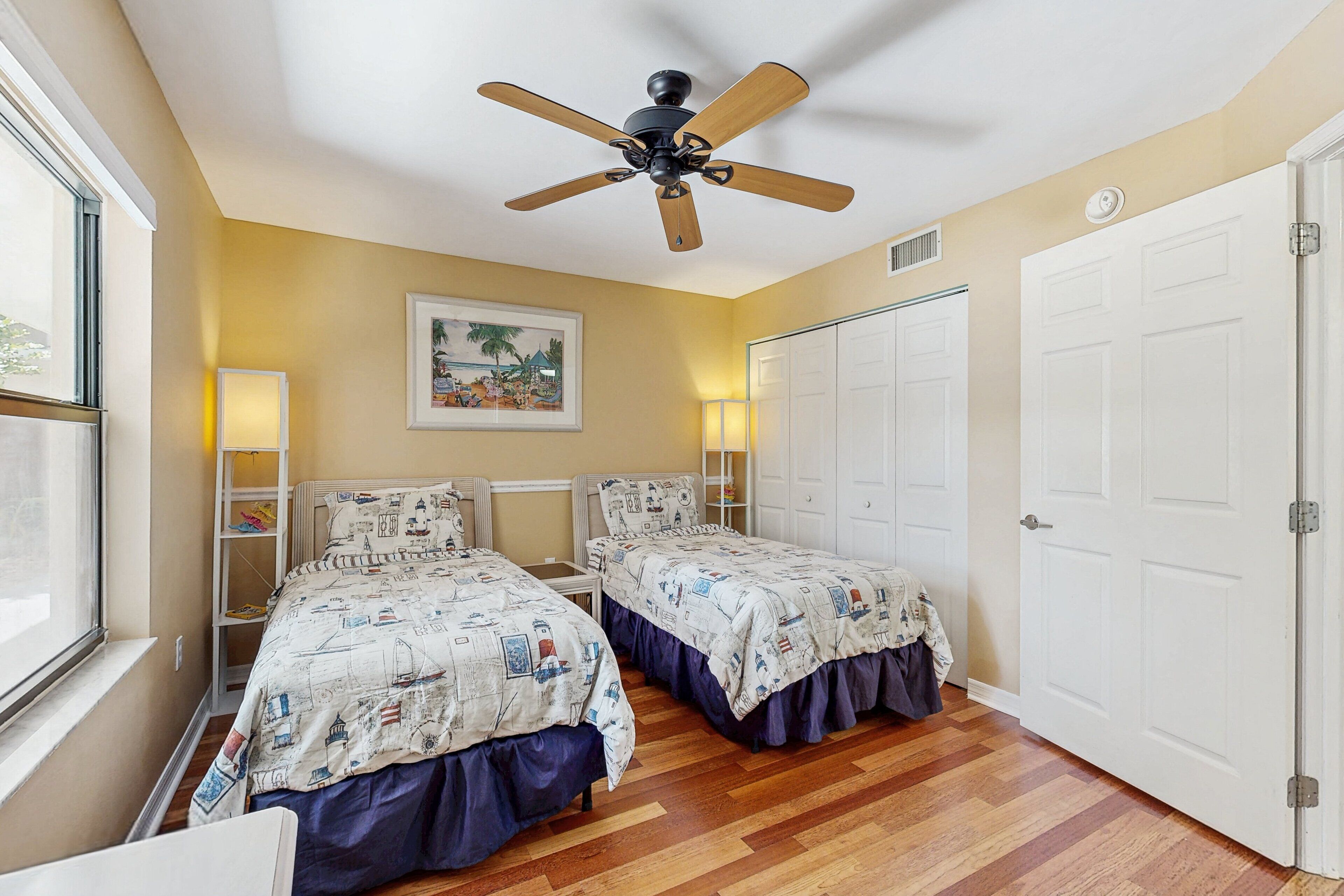 A bedroom with two beds, a ceiling fan, a window, and a door.