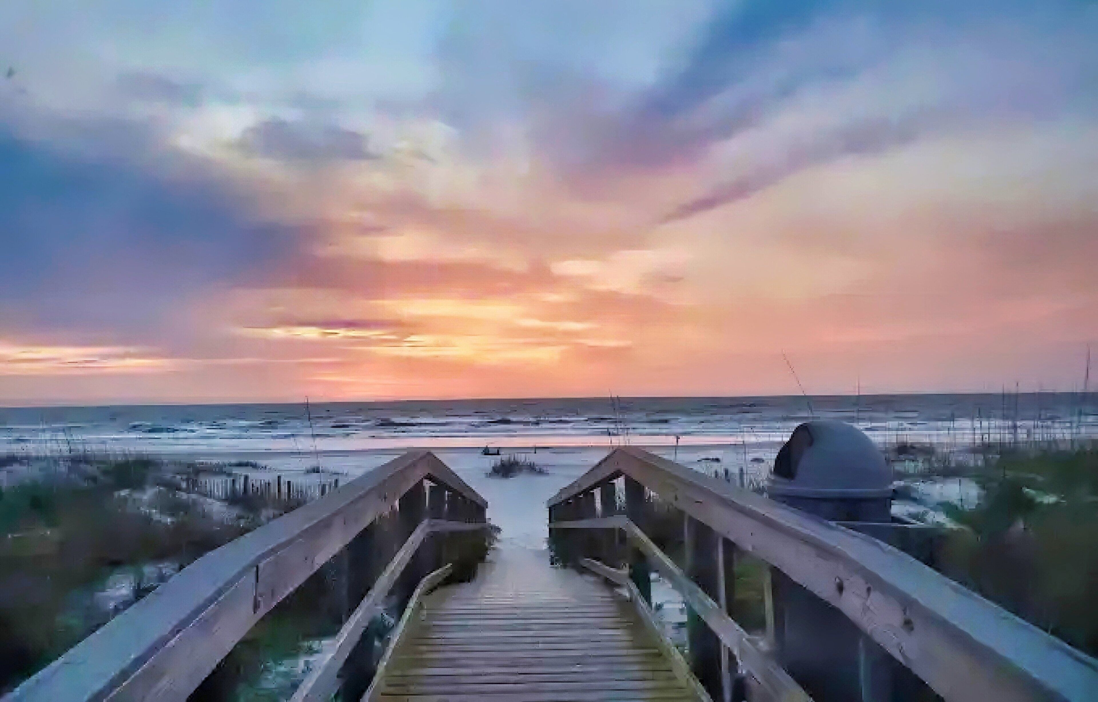 A wooden boardwalk leading to the beach with a sunset in the background.
