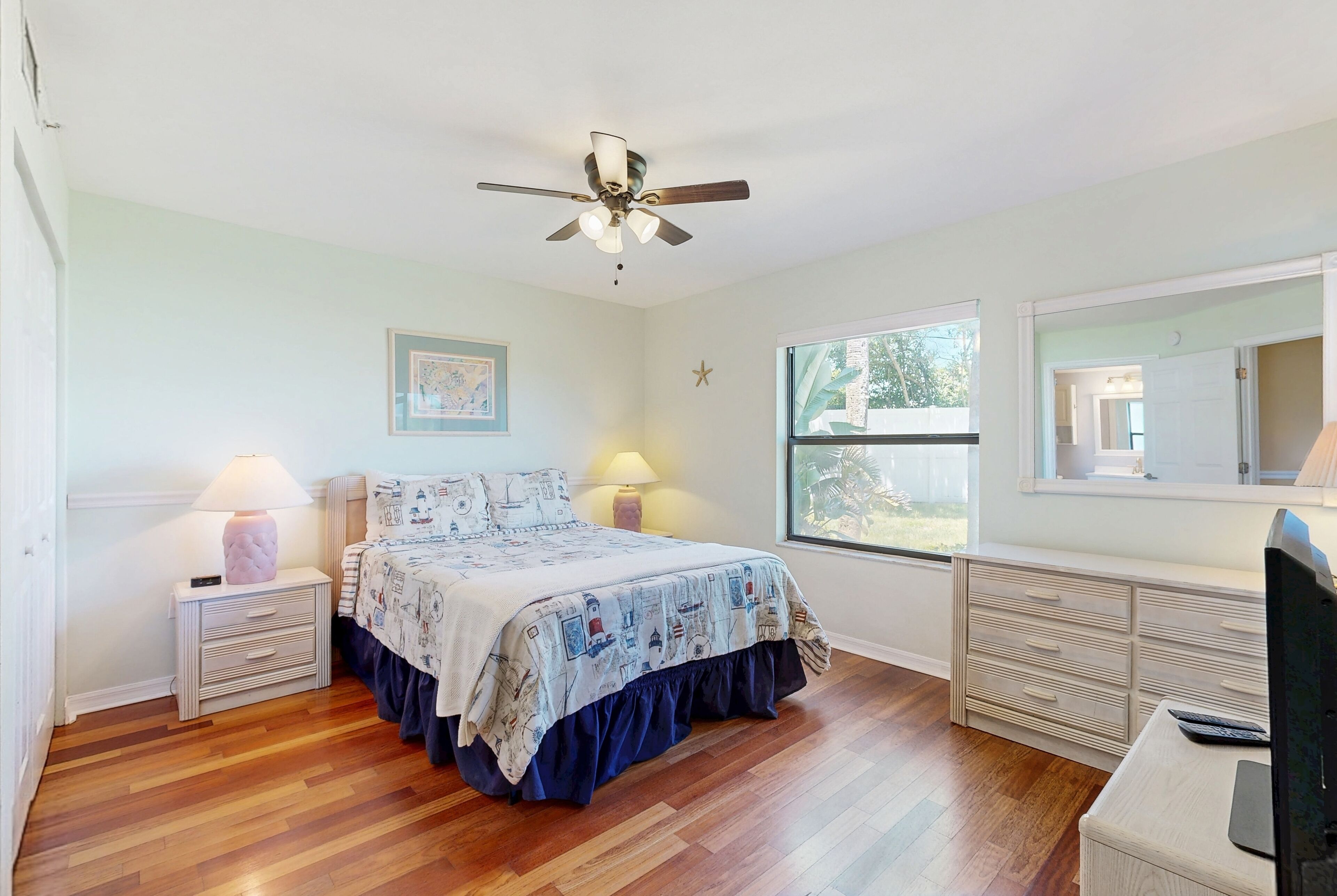 A bedroom with a bed, bedside lamps, a ceiling fan, a dresser, and a window.