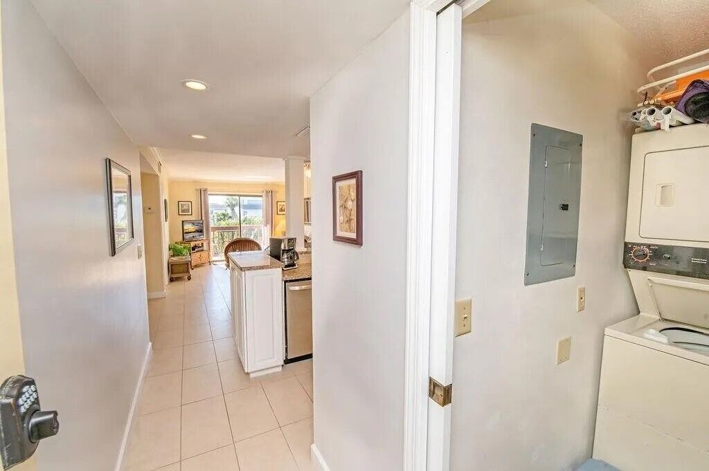 A hallway leading to a kitchen with a refrigerator, a washing machine, and a door with a security camera.