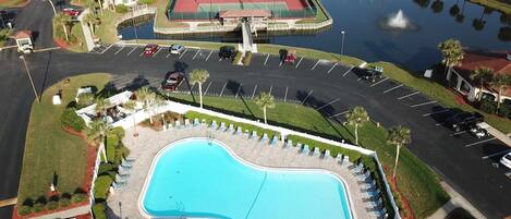 Una piscina con sillones de descanso, cancha de tenis y estacionamiento.