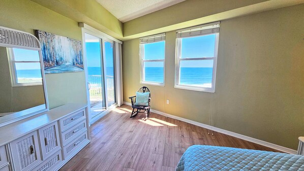 A bedroom with a view of the ocean, a rocking chair, a dresser, and a bed. - Surfclub Retreat 6th Floor Penthouse Corner! Wraparound Balcony! Ocean Views! (Palm Coast)