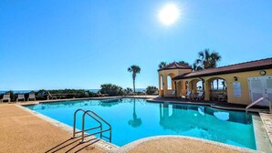 A clear blue pool with a sunlit sky, palm trees, and a building with arches. - Surfclub Retreat 6th Floor Penthouse Corner! Wraparound Balcony! Ocean Views! (Palm Coast)