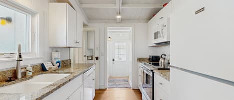 A modern kitchen with white cabinetry, granite countertops, a stainless steel sink, and a built-in oven.