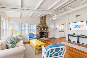 Un ampio soggiorno con camino in pietra, un divano con cuscini decorati, un tavolino da caffè giallo e un televisore che mostra 'Casago Vacation Rentals'.