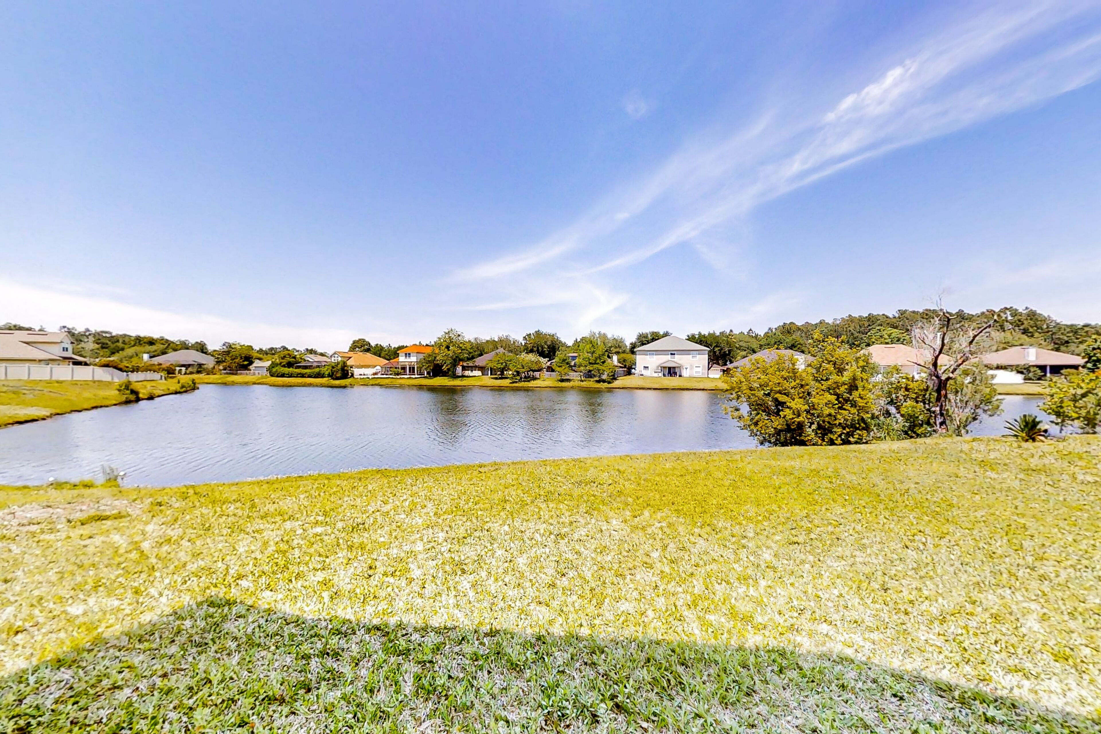 A residential area with a large pond, houses, and a grassy field.