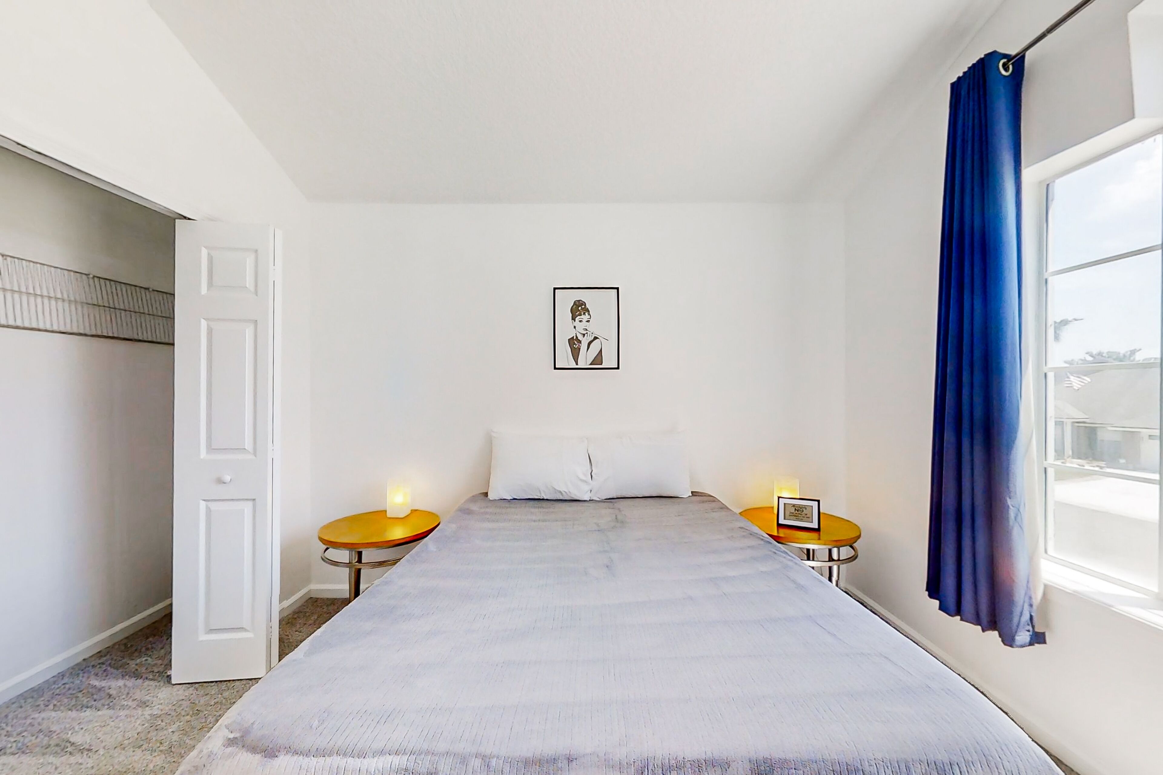 Een slaapkamer met een bed, twee nachtkastjes, een deur, een raam met gordijn, en een lijst met een afbeelding aan de muur.