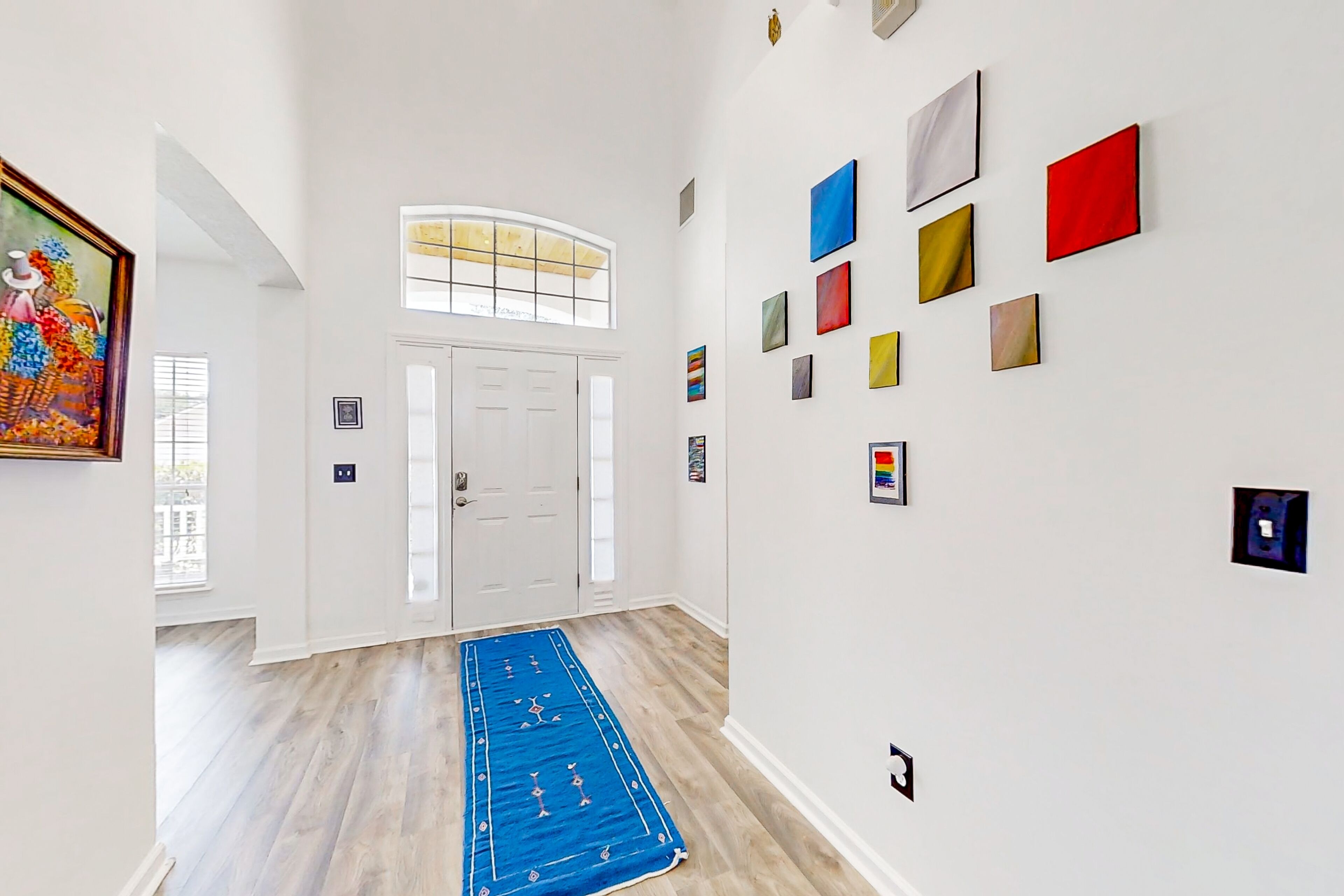 Un couloir avec un tapis bleu, des murs blancs et une porte surmontée d’une fenêtre.
