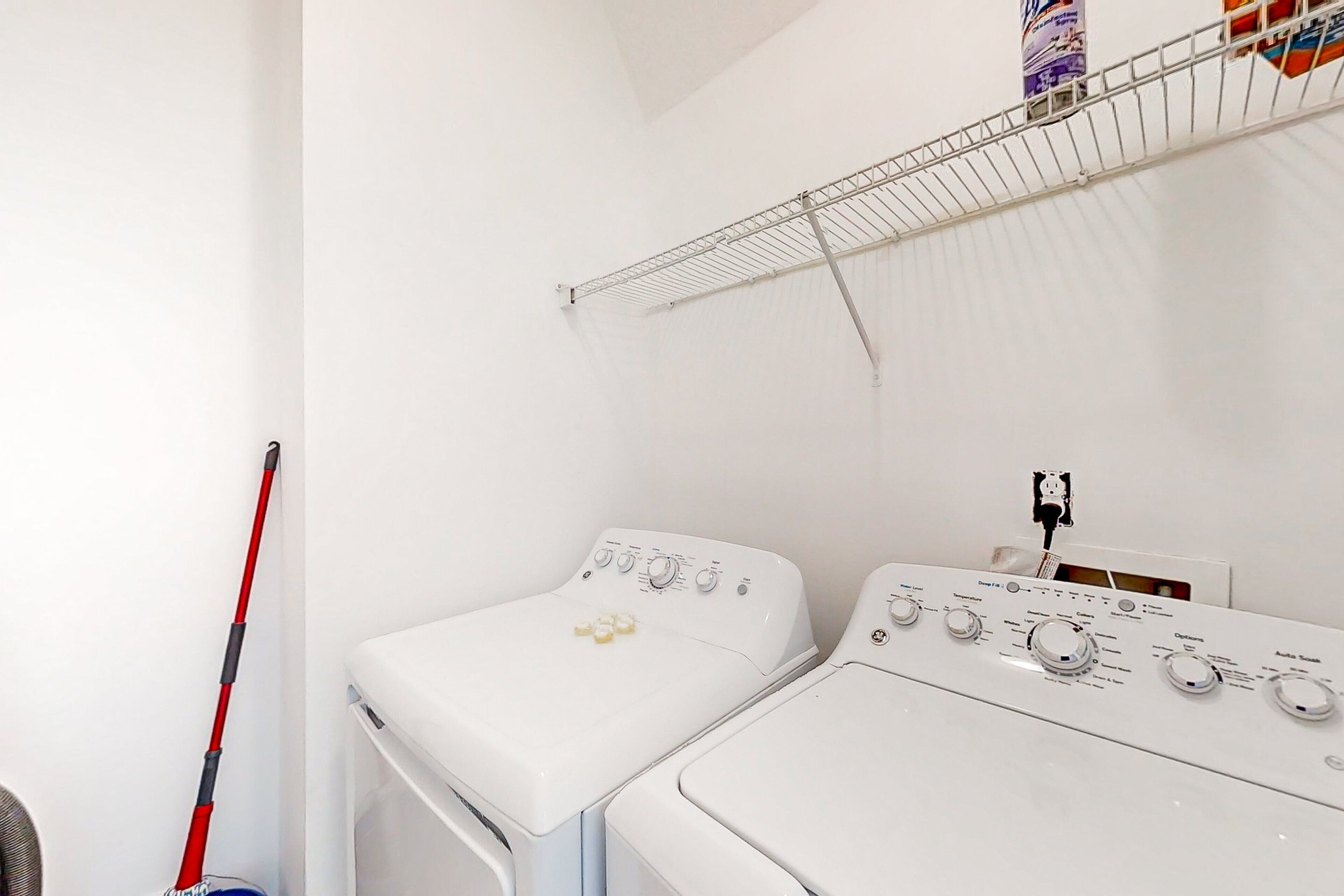 A laundry area with two white washing machines, a red mop, and a metal drying rack.
