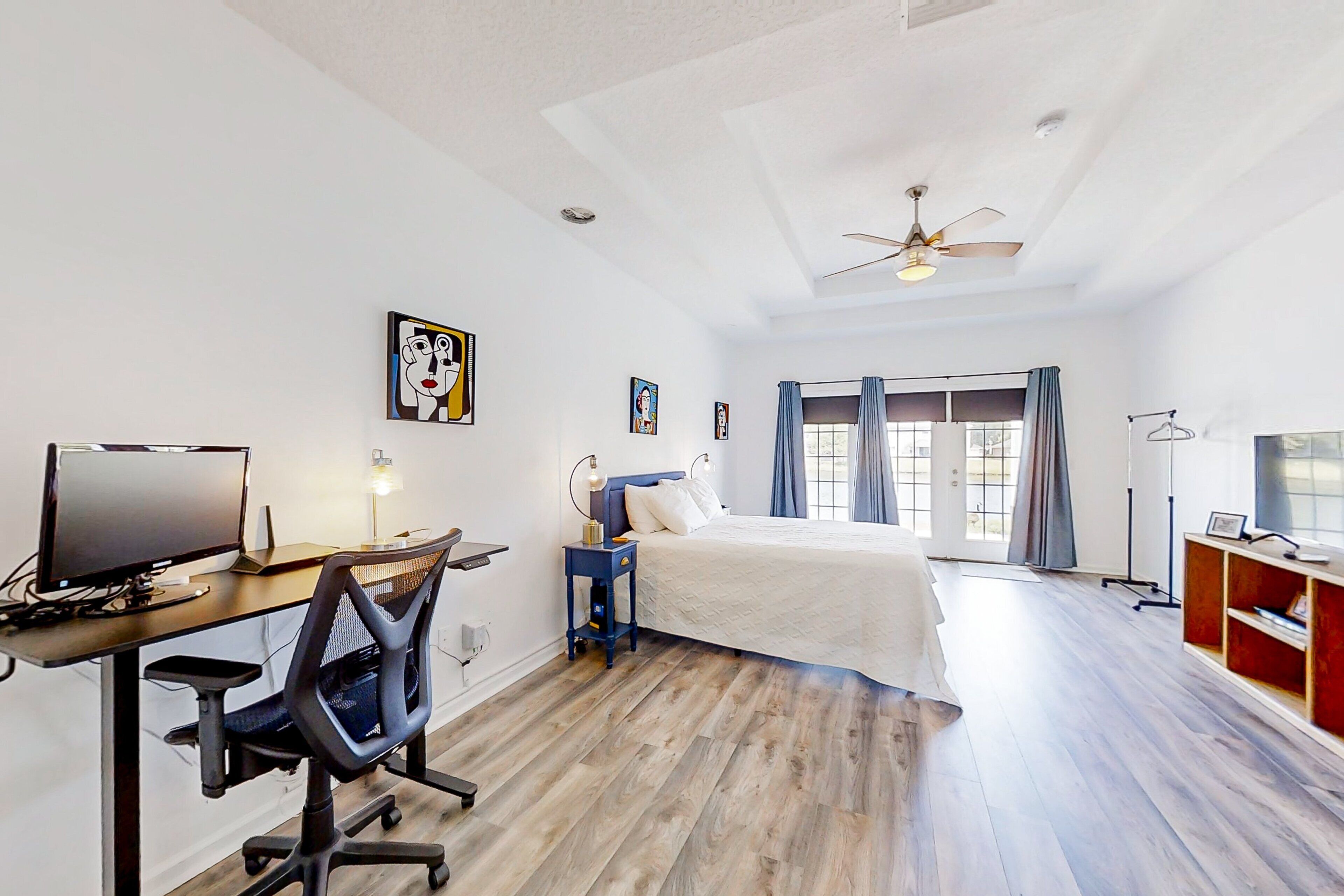 A bedroom with a bed, a desk with a computer, a chair, and a ceiling fan.