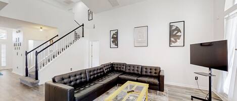 A spacious living room with a sectional sofa, a glass coffee table, and a flat-screen TV.