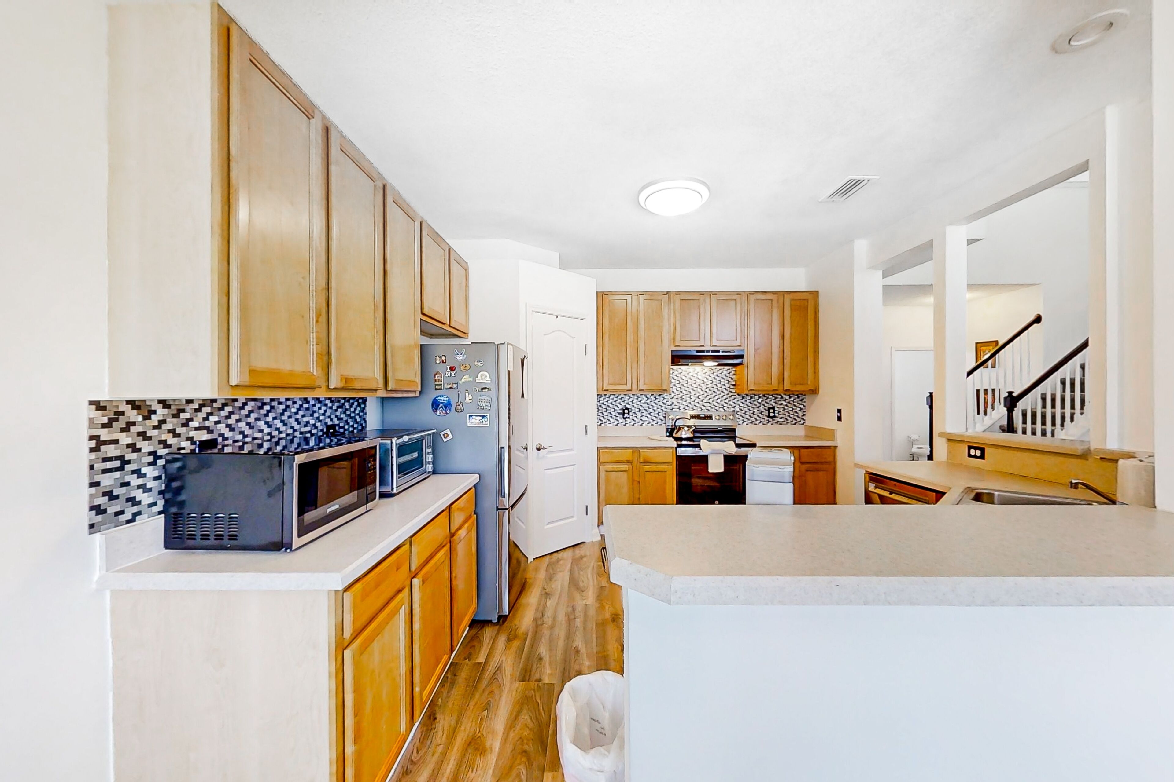 A modern kitchen with wooden cabinets, a microwave, a refrigerator, and a tiled backsplash.