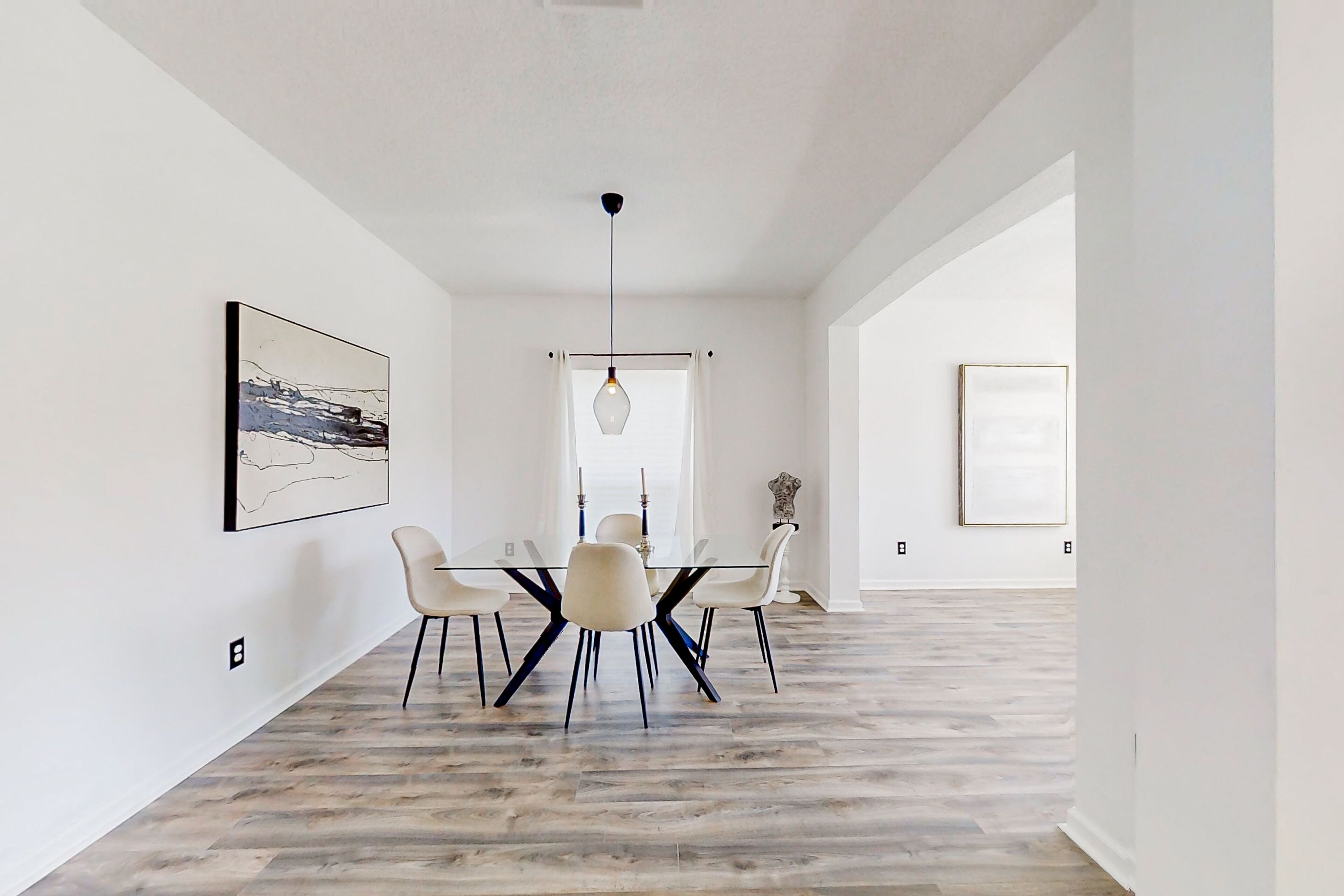 A modern dining area with a glass table, white chairs, and a hanging light fixture.