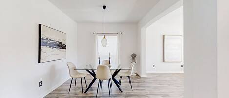 A modern dining area with a glass table, white chairs, and a hanging light fixture.