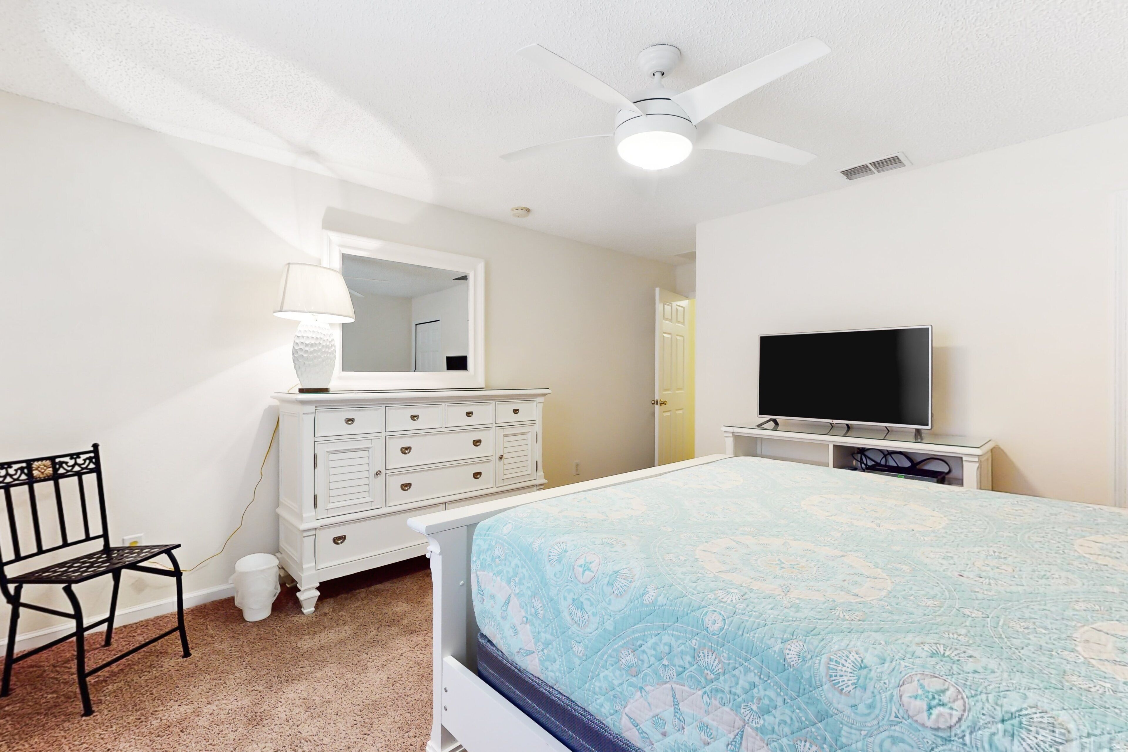 A bedroom with a bed, dresser, TV, and a chair.