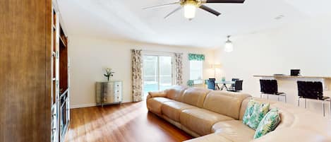 A spacious living room with a large leather sofa, wooden flooring, and a ceiling fan.
