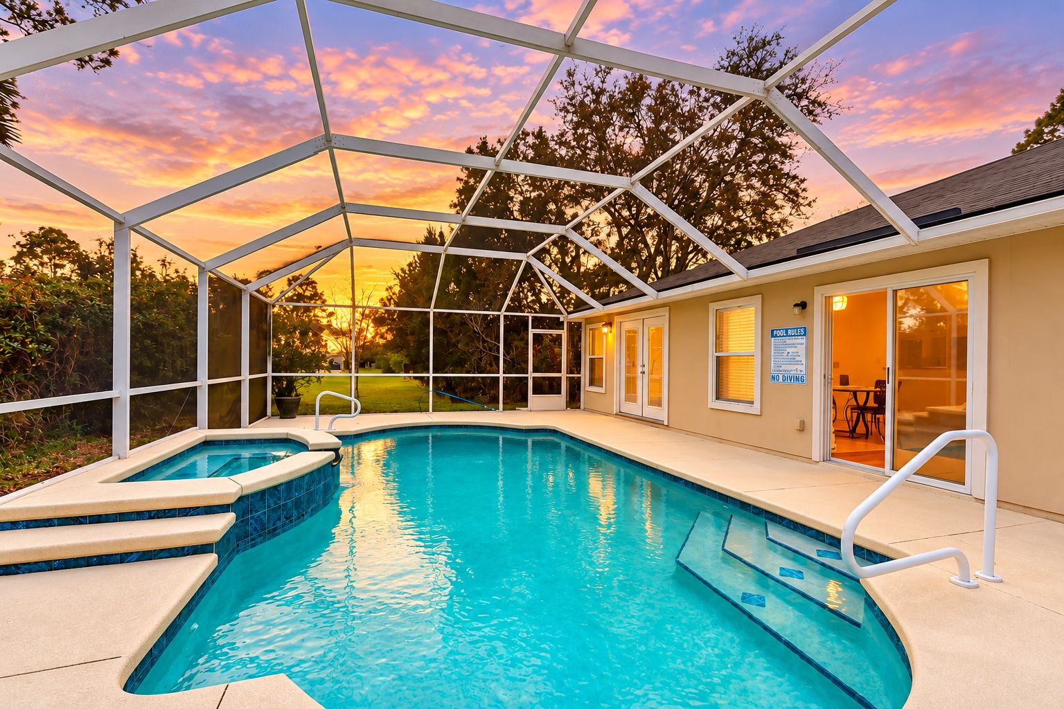 A swimming pool with a covered area, a hot tub, and a patio with a view of the sunset.