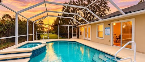 A swimming pool with a covered area, a hot tub, and a patio with a view of the sunset.