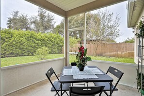 A covered patio with a table and chairs, a potted plant, and a view of a backyard with a wooden fence and greenery. - Wonderful Coastal Home With Wifi, Enclosed Backyard, Screened Patio (Palm Coast)