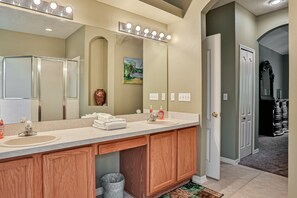 A bathroom with a large vanity, a mirror with lights, a sink, and a door leading to another room. - Wonderful Coastal Home With Wifi, Enclosed Backyard, Screened Patio (Palm Coast)