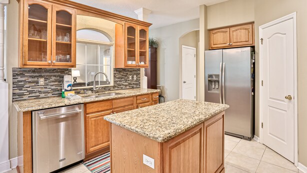 A modern kitchen with wooden cabinets, granite countertops, stainless steel appliances, and a tiled backsplash. - Wonderful Coastal Home With Wifi, Enclosed Backyard, Screened Patio (Palm Coast)