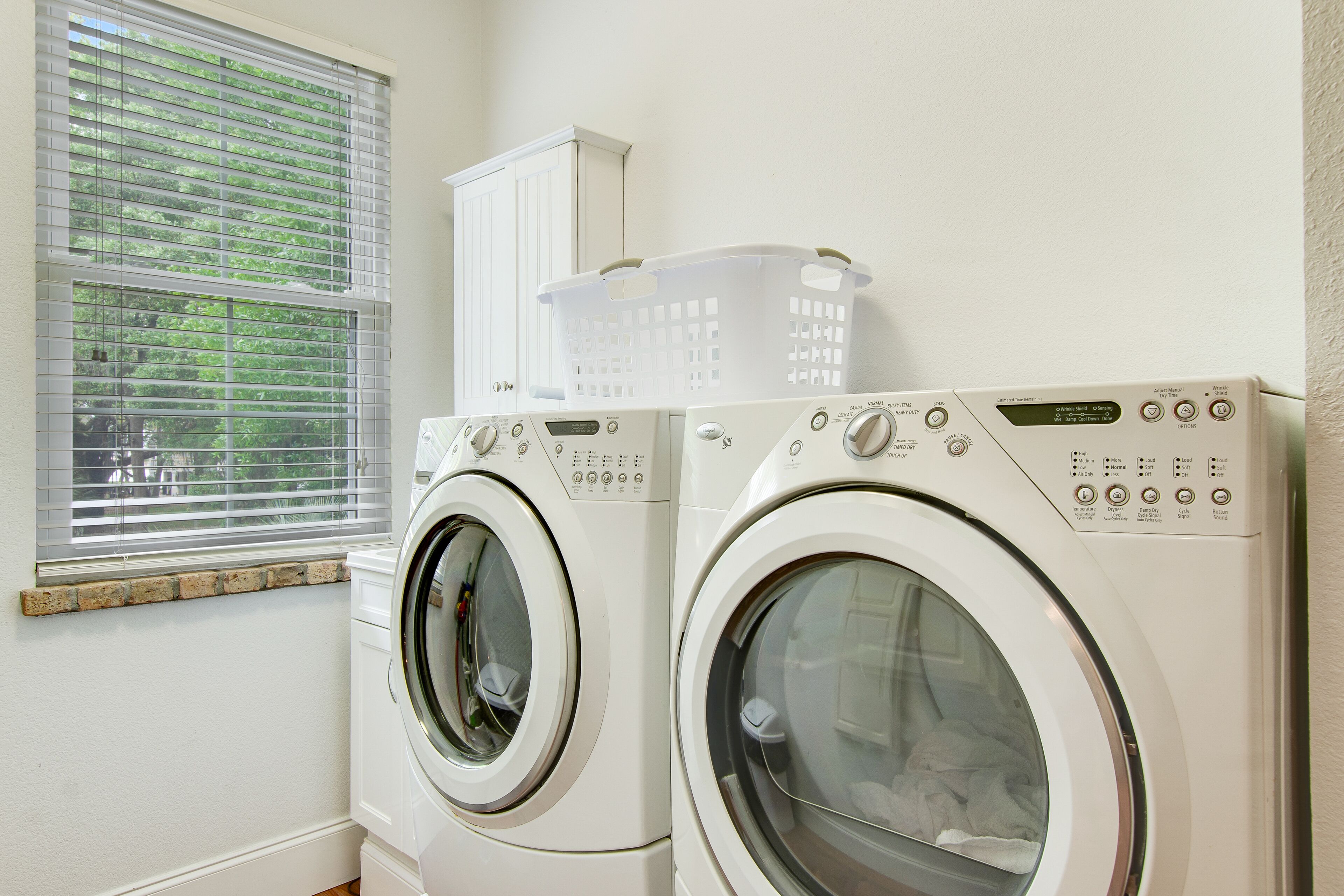 A laundry room with two front-loading washing machines and a window with blinds.