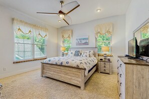 Un dormitorio con cama de madera, ventilador de techo, cómoda y televisor.