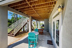Un patio cubierto con techo de madera, mobiliario exterior y una escalera que lleva a un nivel superior.