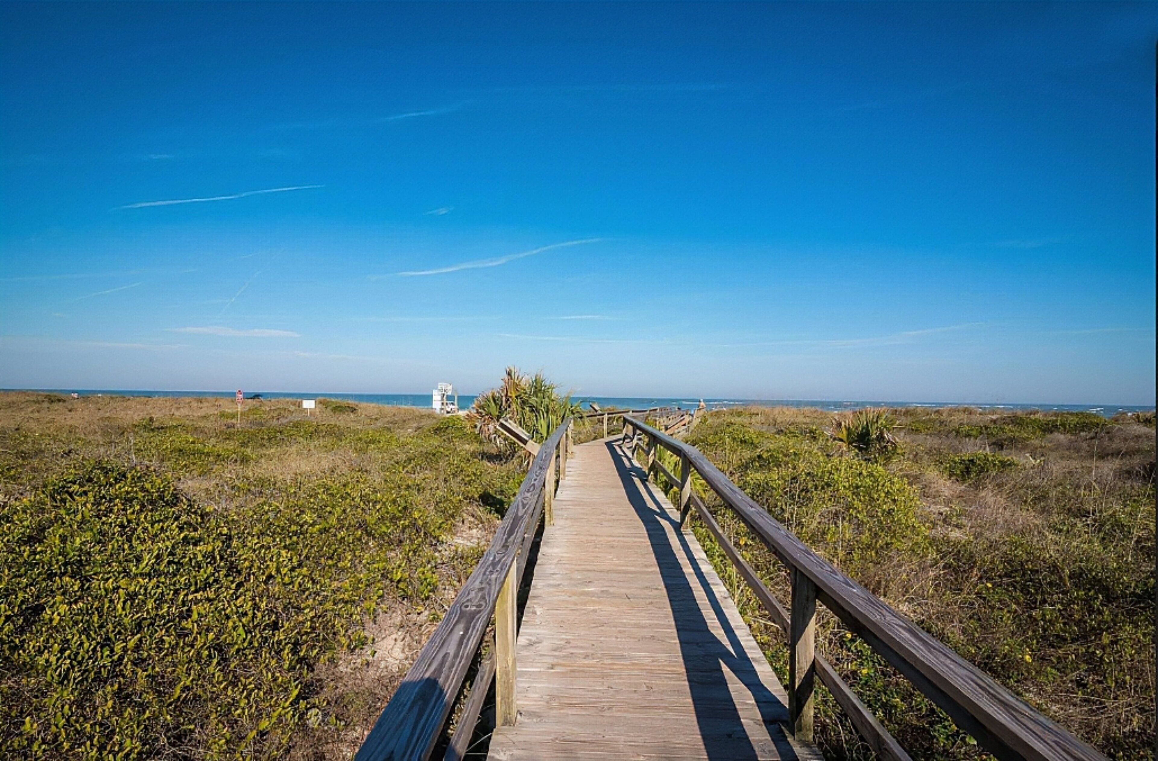 A wooden boardwalk leading to a beach with a clear sky.