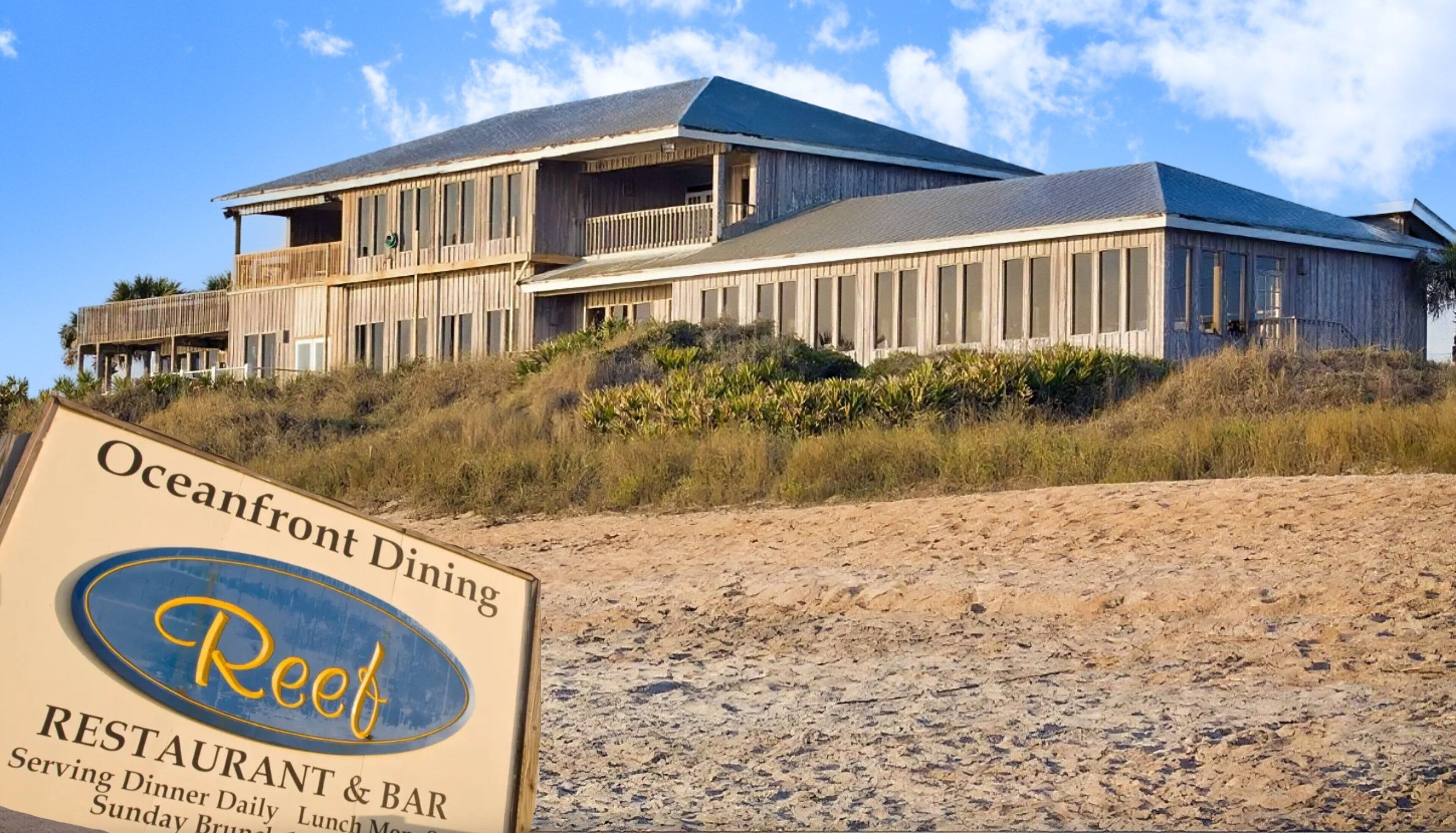Un restaurante frente a la playa llamado Reef, con un edificio grande y varias terrazas, y una playa de arena en primer plano.