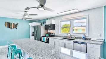 A modern kitchen with granite countertops, stainless steel appliances, teal bar stools, and a large window with a view.