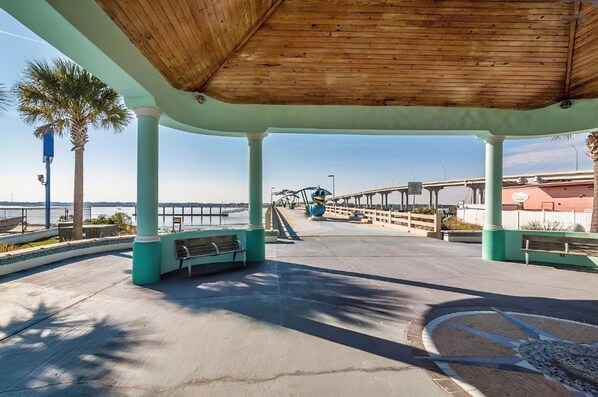 A covered walkway with benches, palm trees, and a view of the water and bridge. - Sunny Upper Level 1 Block From 2 Beaches W/private Pool, High-speed Wi-fi (St. Augustine)