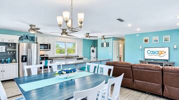 A modern kitchen with stainless steel appliances, a dining area with a blue table, and a living area with a brown sofa.