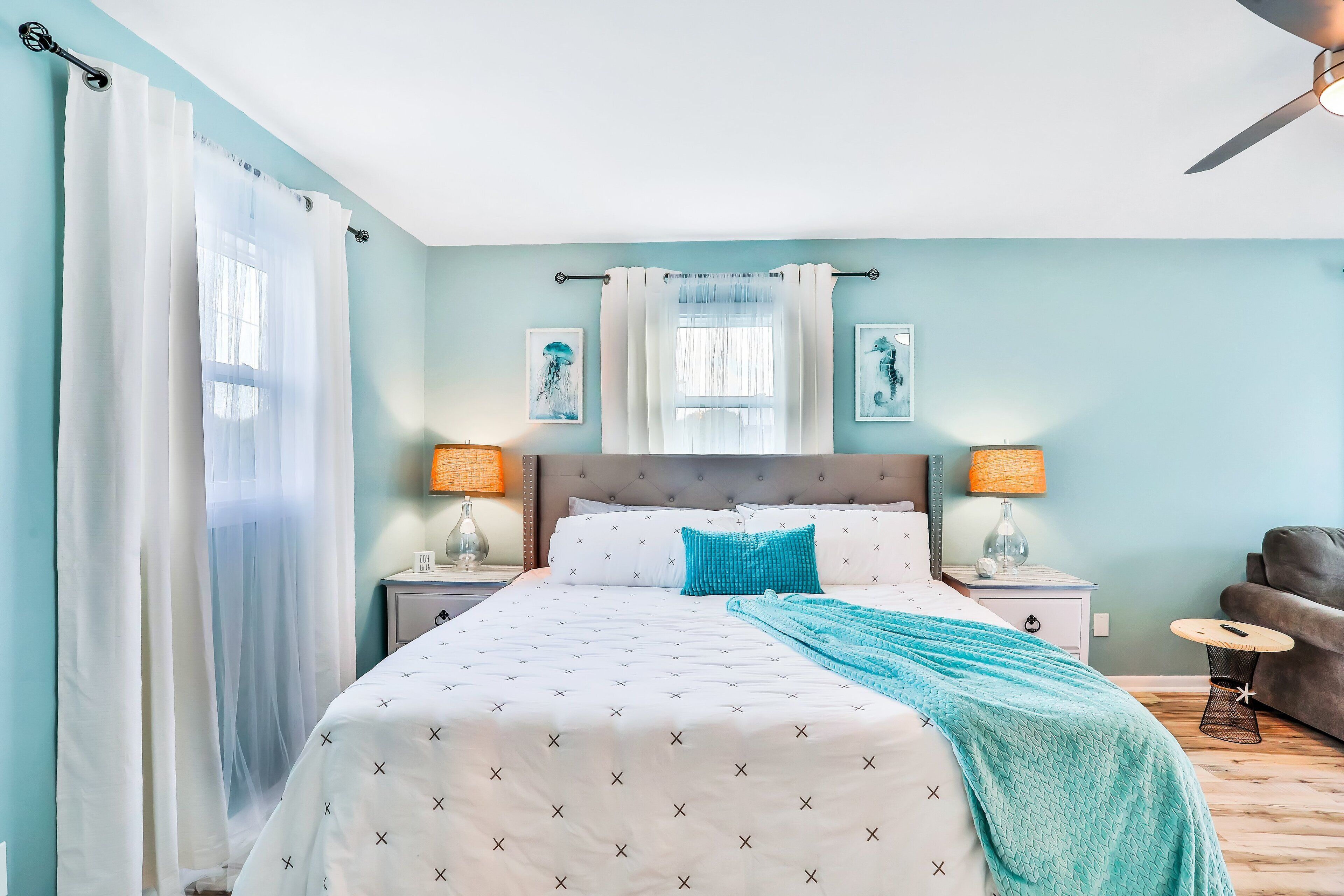 Une chambre à coucher avec un lit, deux tables de chevet avec des lampes, un canapé gris et une fenêtre avec des rideaux.