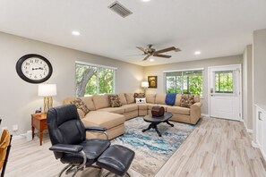 A living room with a sectional sofa, a black leather chair, a coffee table, a clock, and a ceiling fan. - Updated House With Enclosed Yard, Patio, Central AC, & Washer/dryer (Jacksonville)