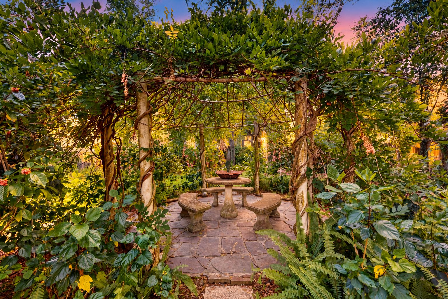 A garden with a stone bench and a table under a vine-covered pergola.