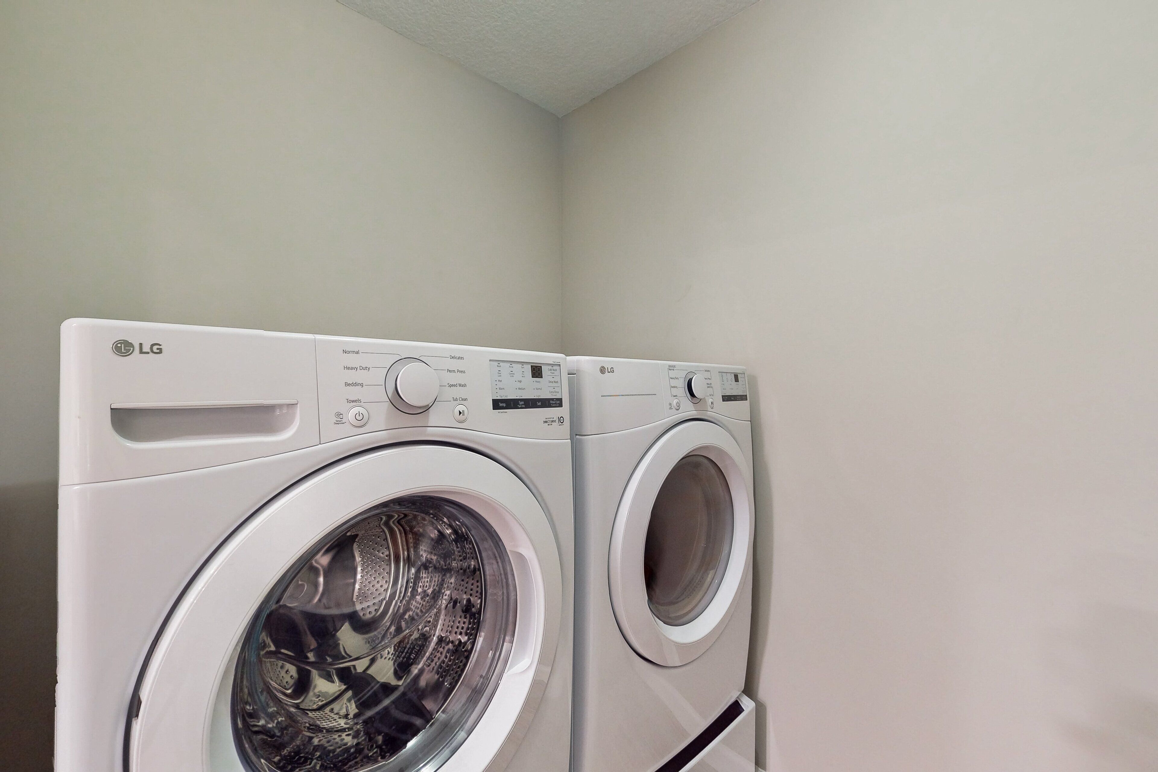 Two LG front-loading washing machines in a corner of a room with plain walls.