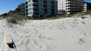Un hotel frente a la playa con varios pisos, balcones y una playa arenosa en primer plano.