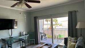 Una sala de estar con televisor, mesa de centro de madera y sofá. Hay un balcón con vistas a la playa.