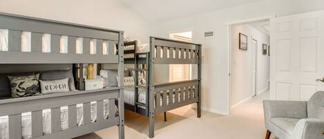 A room with two bunk beds, a gray armchair, and a white door.