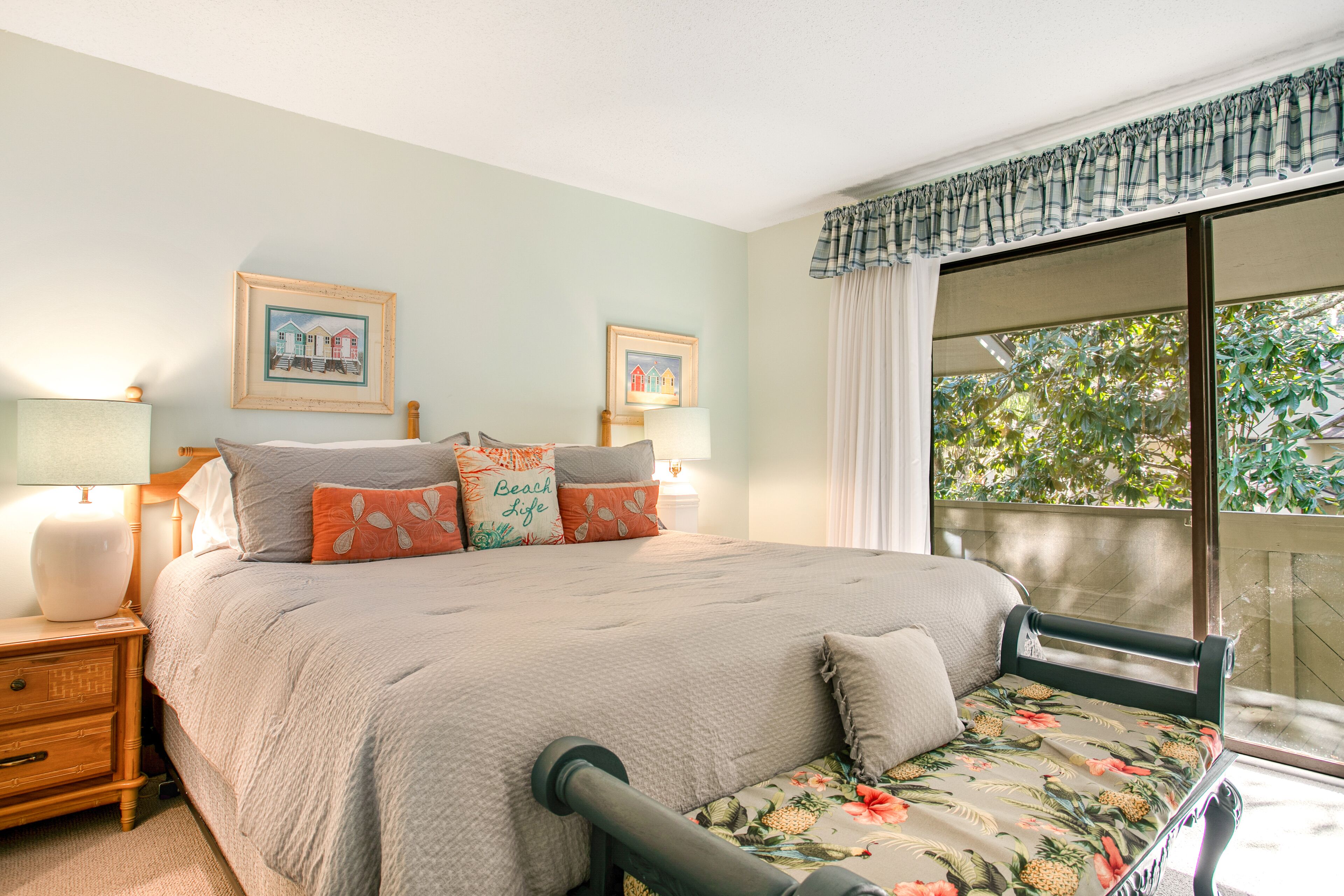 A bedroom with a bed, two bedside tables with lamps, a window with curtains, and two framed pictures on the wall.