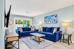 A living room with two blue sofas, a glass coffee table, and a wooden side table. - Water-view Dog-friendly Home With Outdoor Space & Entertainment Options (Palm Coast)
