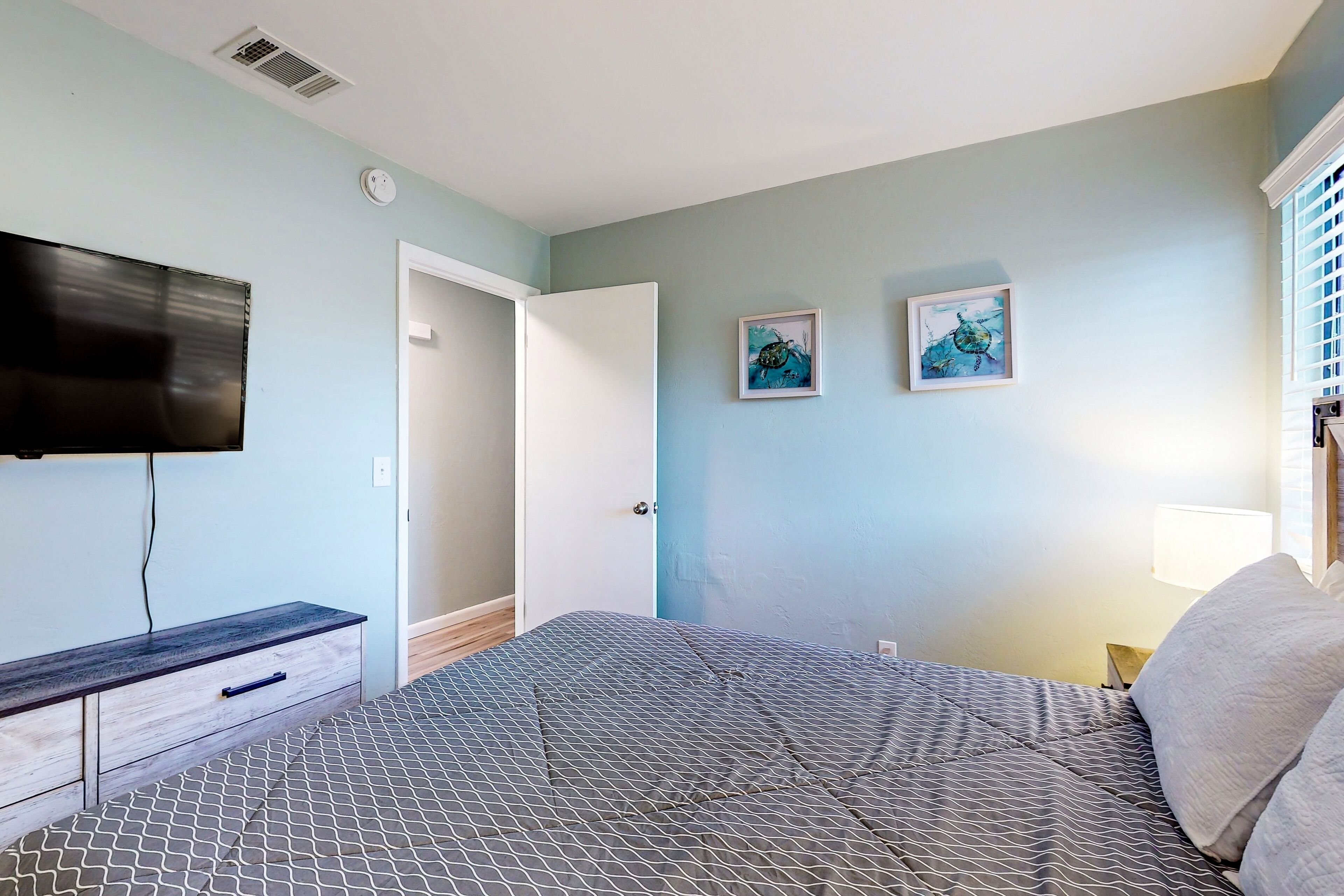 A bedroom with a bed, a TV mounted on the wall, a bedside table, and two framed pictures on the wall.