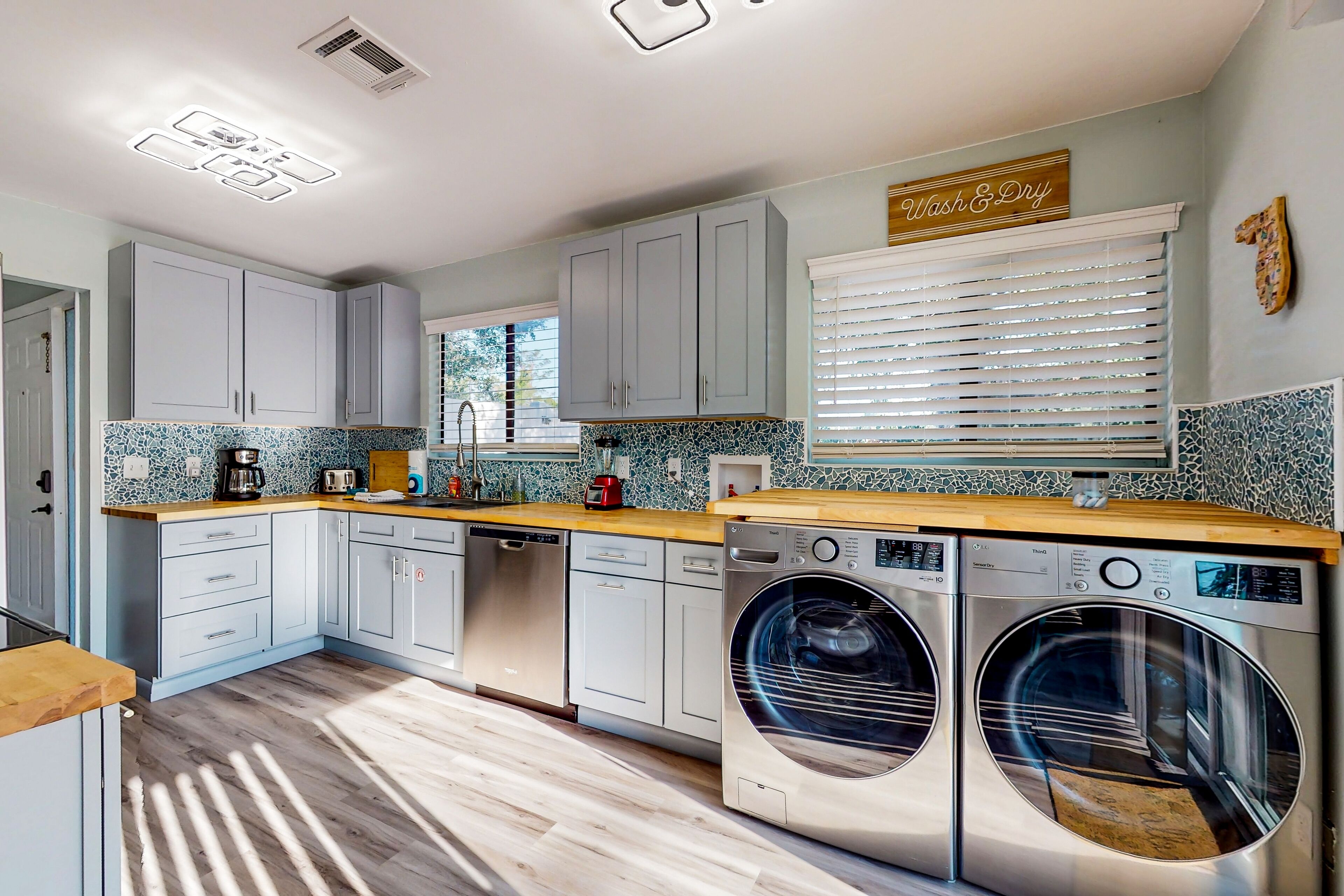 A modern kitchen with grey cabinets, a wooden countertop, a washing machine, and a window with blinds.