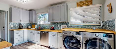 A modern kitchen with grey cabinets, a wooden countertop, a washing machine, and a window with blinds.