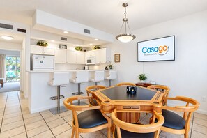 Une cuisine moderne avec des meubles blancs, un coin repas avec une table et des chaises en bois, et un écran fixé au mur qui affiche « Casago Vacation Rentals ».