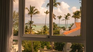 Blick aus dem Fenster auf einen Strand mit Palmen und blauem Himmel.