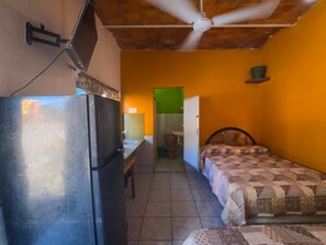 Une pièce de taille modeste comprenant un lit, un petit bureau, un réfrigérateur et un ventilateur de plafond.