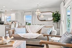 A living room with a sofa, a coffee table, a chandelier, a mirror, and a view of the outside. - Steps to the beach! Perfect Location Seagrove area.  3BR 2 bath, 2Pool, sleeps 8 (Santa Rosa Beach)
