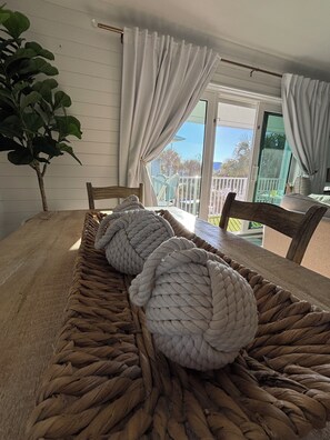 A room with a wooden dining table, two large woven poufs, a potted plant, and a view of the outdoors through a sliding glass door. - Steps to the beach! Perfect Location Seagrove area.  3BR 2 bath, 2Pool, sleeps 8 (Santa Rosa Beach)